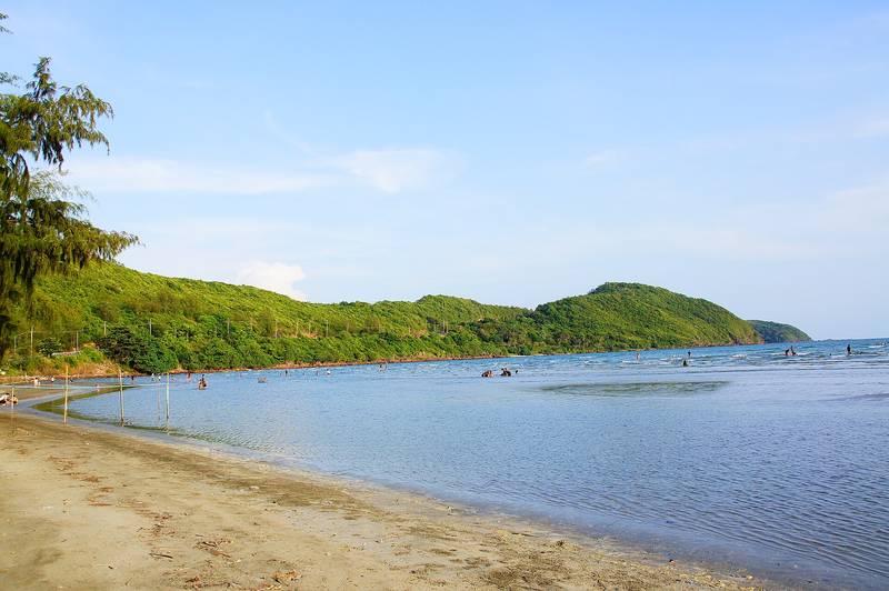 หาดทรายริมทะเลน้ำใส มีแนวเขาเขียวยื่นลงทะเลใต้ฟ้าสีฟ้า